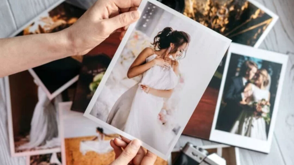 Printed wedding photos with the bride and groom, a vintage black camera and woman hands with photo
