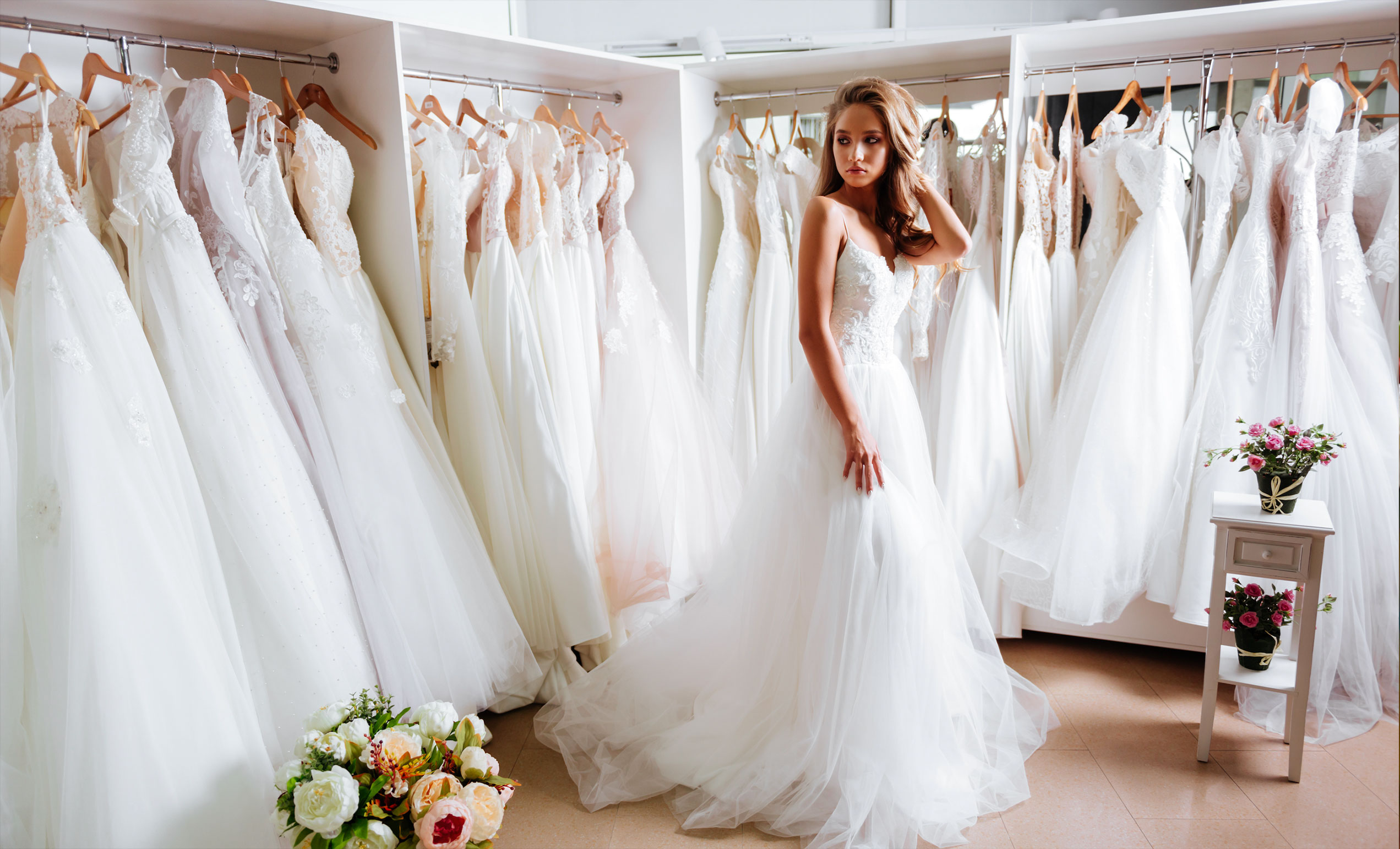 Back view of a young woman in wedding dress looking at bridal gowns on display in boutique