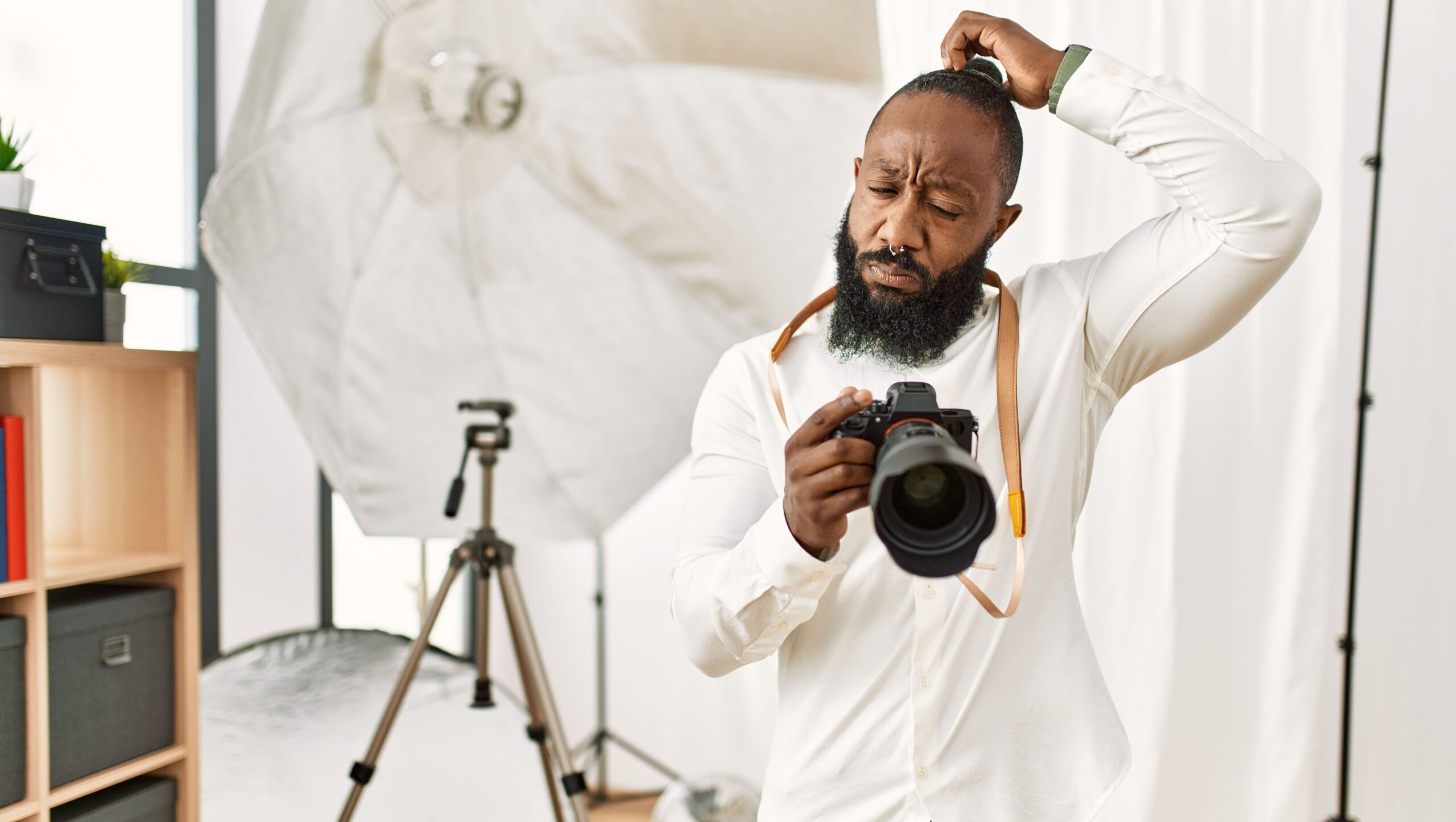 american photographer man working at photography studio confuse and wondering about question. uncertain with doubt, thinking with hand on head.